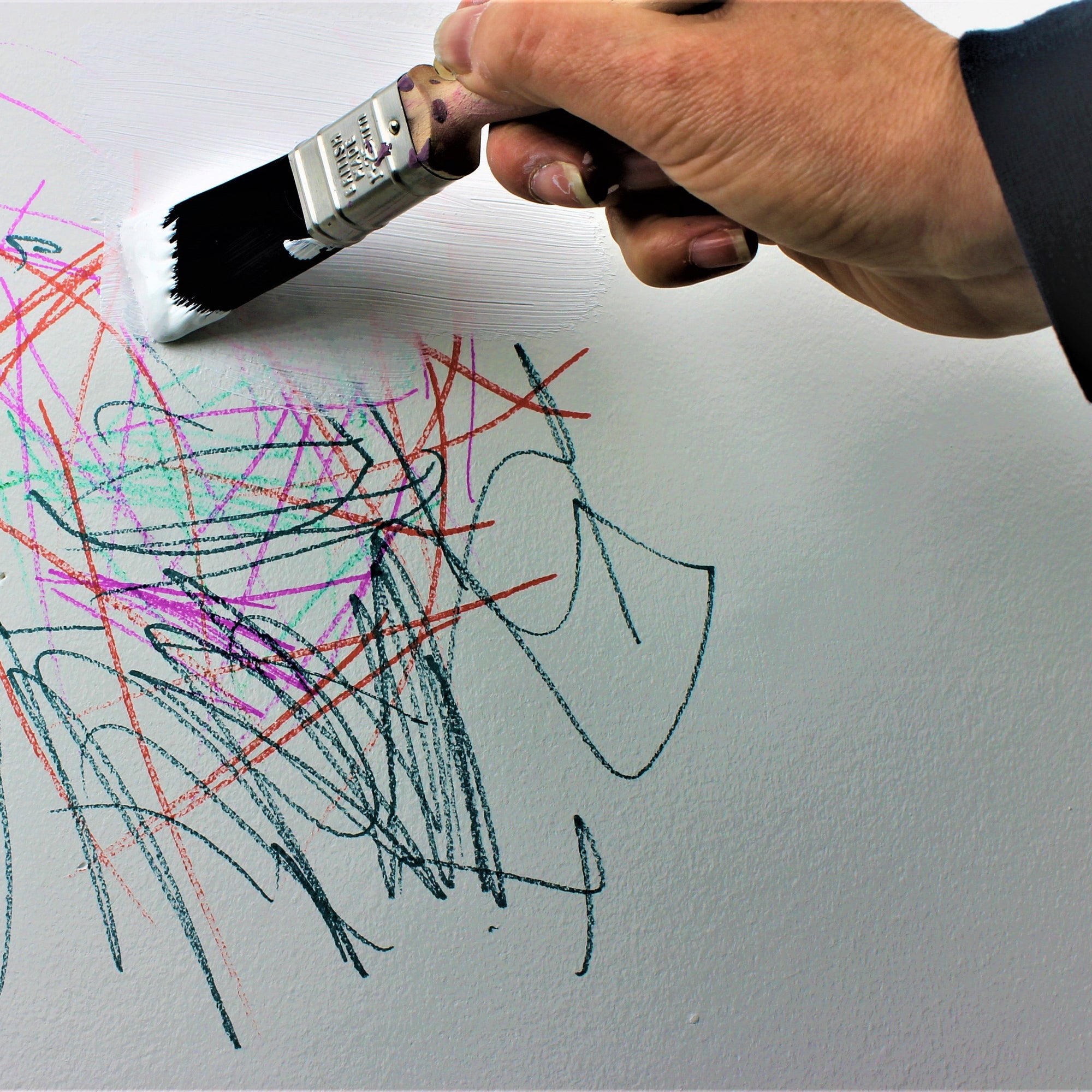 man applying primer over a child's scribbles on a wall